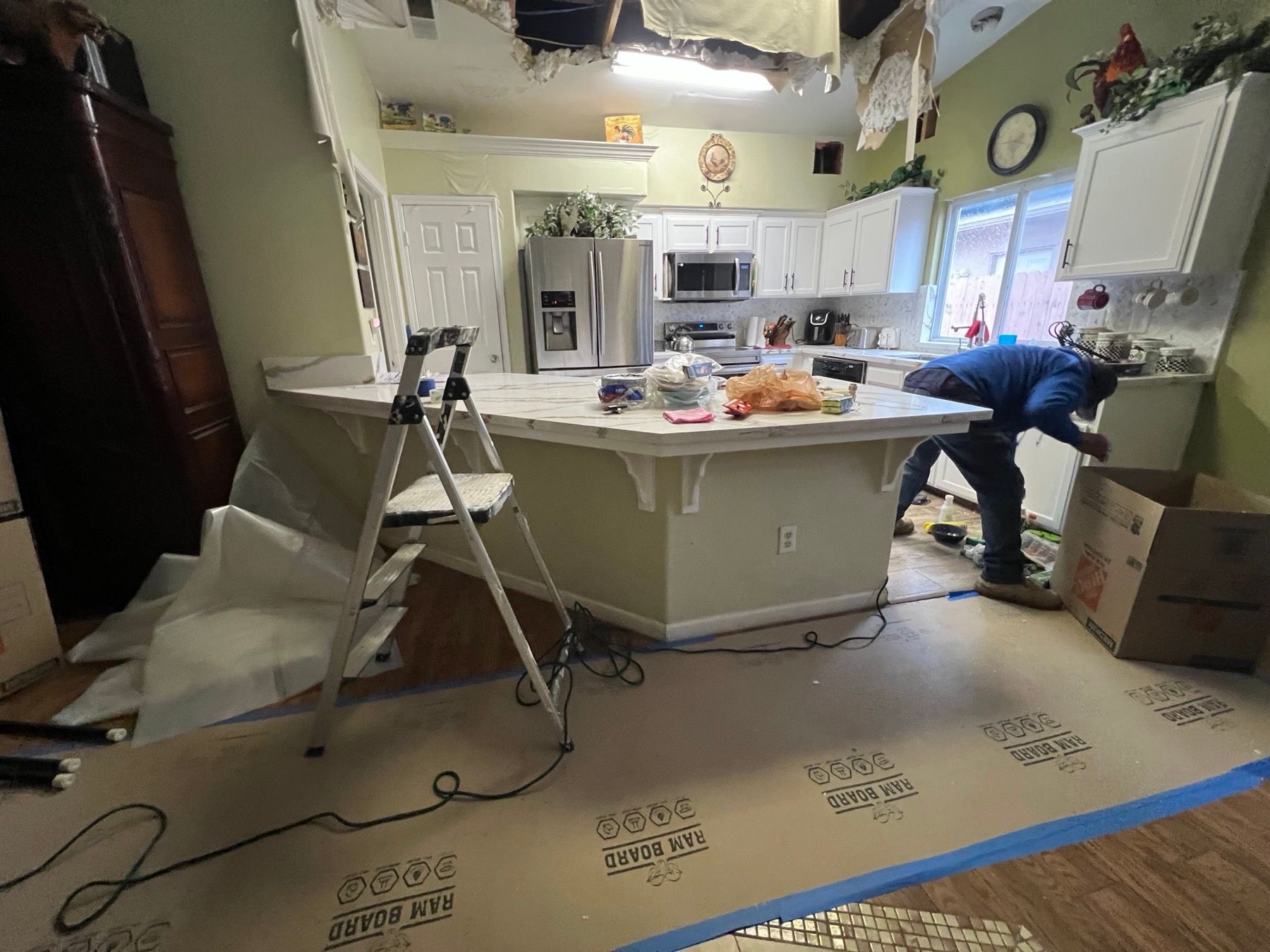 Technician working in a kitchen with the ceiling opened after a leak, floor protection taped down